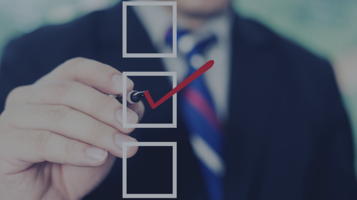Close-up of a businessperson in a suit marking a checklist, drawing a red check mark inside a square box.