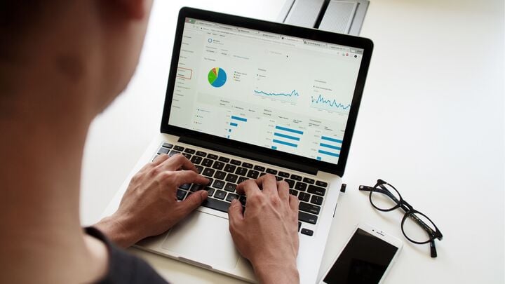 man standing over a laptop with graphs and charts on the screen