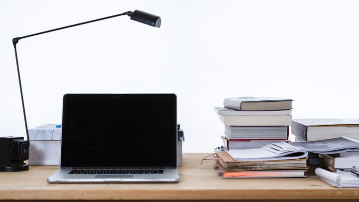 Laptop on a table next to a stack of books