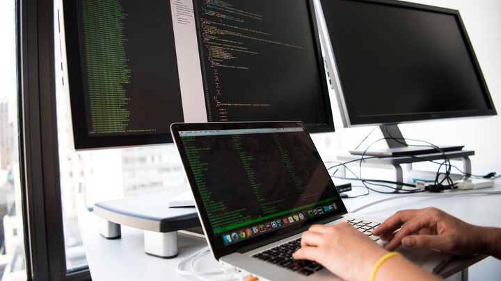 Developer working on a laptop with multiple external monitors displaying code in a multi-screen programming workspace setup