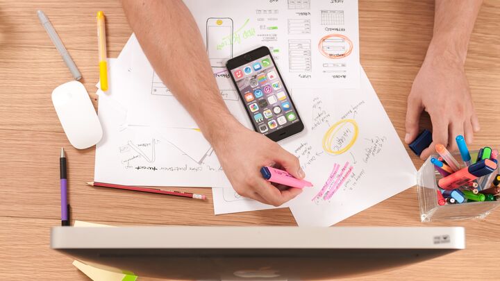 Papers and a phone laying across a table, a hand holding a highlighter over the papers