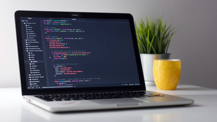 Open laptop showing software development code on a dark-themed text editor, placed on a minimalist workspace with a decorative plant in a yellow pot