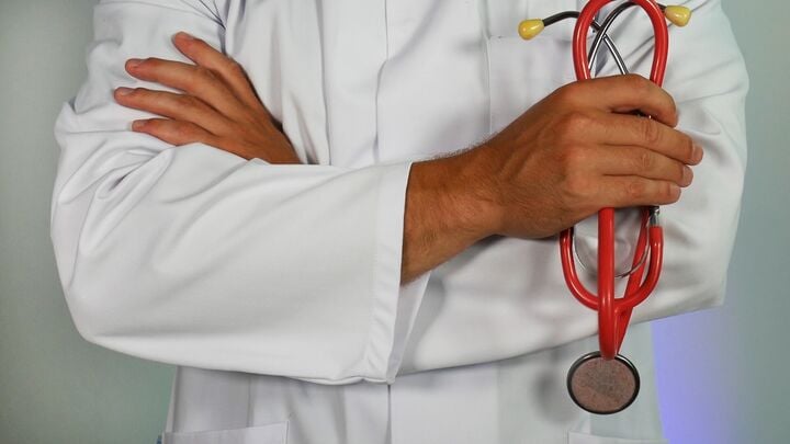 Healthcare professional in white coat holding a red stethoscope with arms crossed.