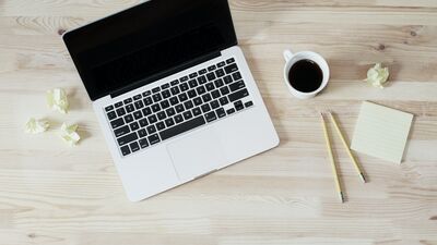 Open laptop surrounded by a coffee cup, pencils, and crumpled Post-It notes