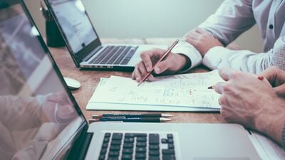 Two peoples' arms on a desk looking at spreadsheets