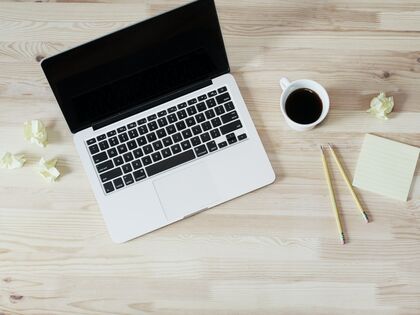 Open laptop surrounded by a coffee cup, pencils, and crumpled Post-It notes