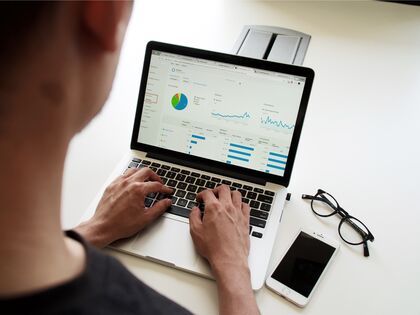 man standing over a laptop with graphs and charts on the screen