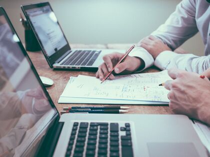 Two peoples' arms on a desk looking at spreadsheets