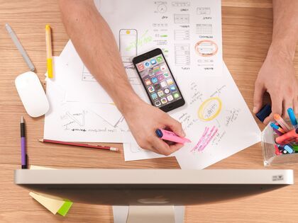 Papers and a phone laying across a table, a hand holding a highlighter over the papers