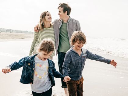 Happy Family of Four Walking Together on the Beach