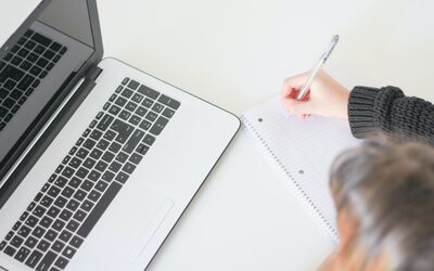 woman writing in a notebook with a laptop next to her