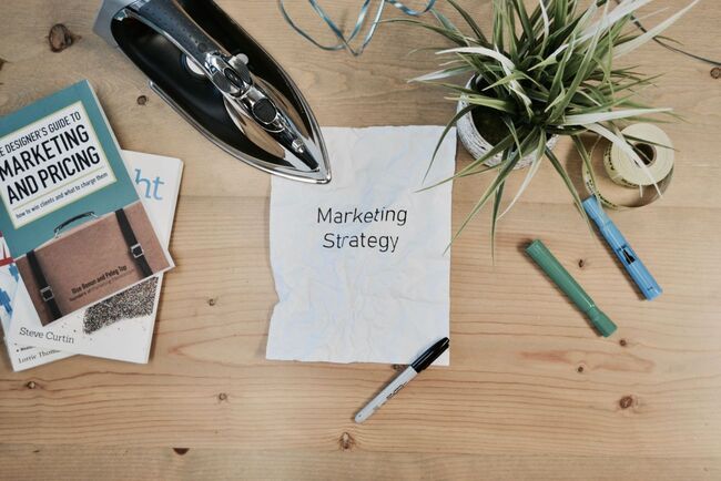 Image of messy desk with paper that says "Marketing Strategy" on it