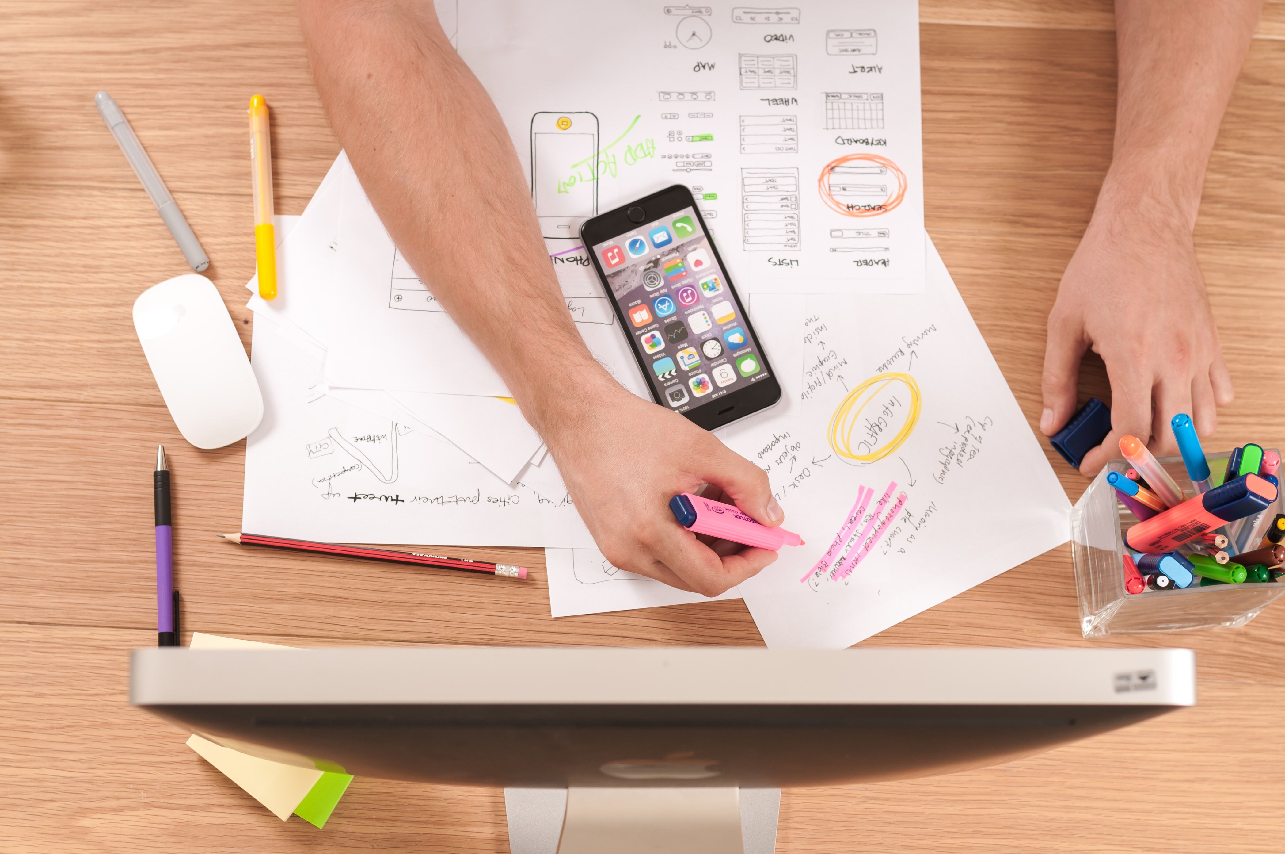 Papers and a phone laying across a table, a hand holding a highlighter over the papers