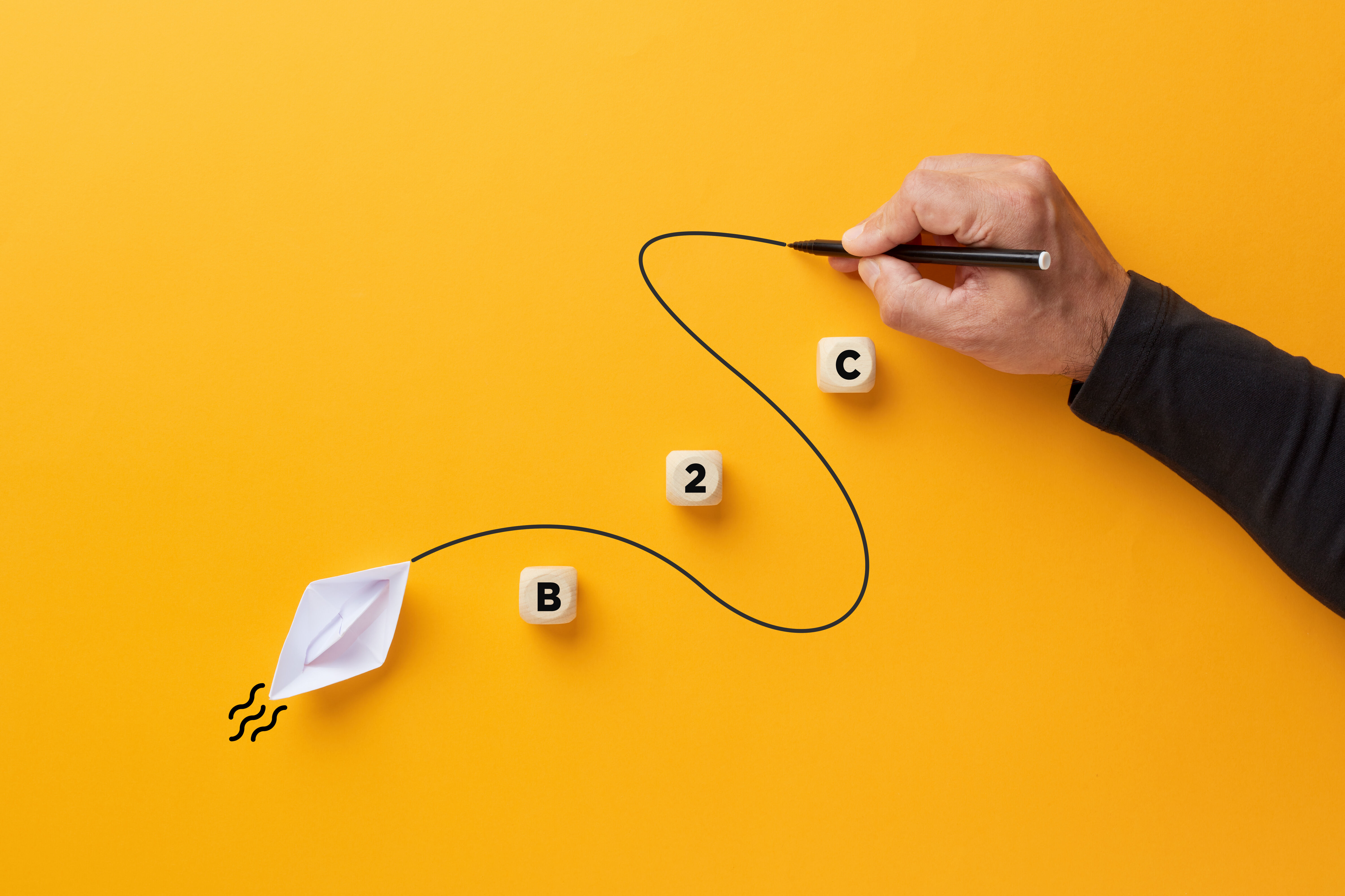 Male hand draws a curved line that guides a paper boat with the acronym B2C