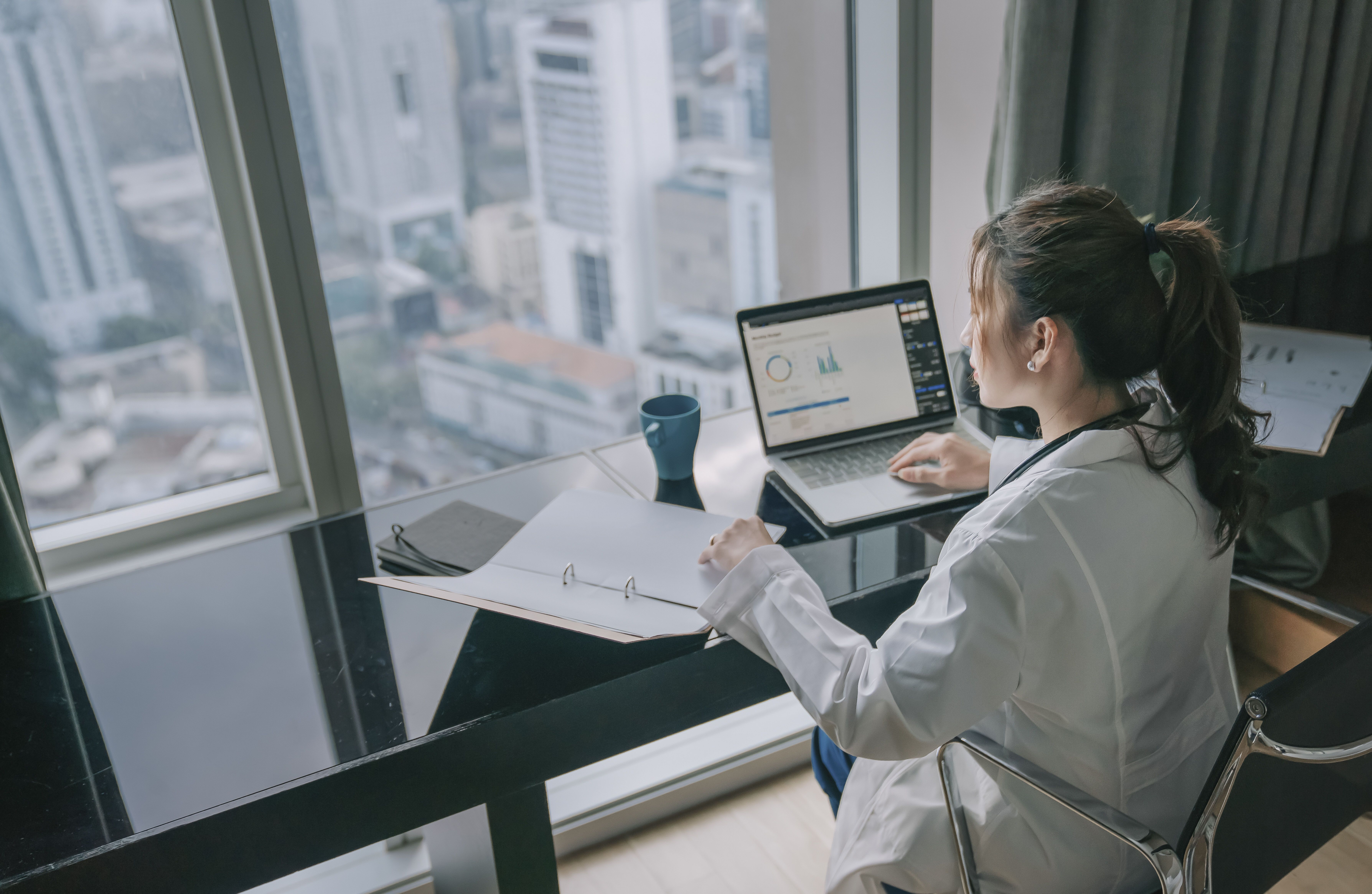 female doctor working on medical report with laptop and document file